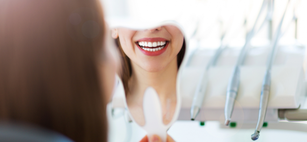 Young woman looking at her new smile in a handheld mirror.